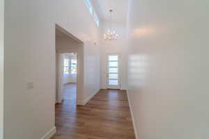 Hallway with high vaulted ceiling, hardwood / wood-style floors, and a chandelier