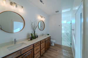 Bathroom featuring dual vanity, toilet, a shower with door, and hardwood / wood-style floors