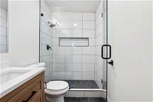 Bathroom with toilet, vanity, an enclosed shower, and tile floors