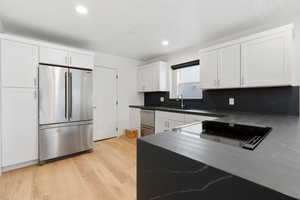 Kitchen with stainless steel built in refrigerator, tasteful backsplash, light hardwood / wood-style floors, and white cabinets