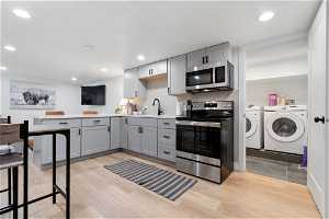 Kitchen featuring appliances with stainless steel finishes, washer and dryer, light hardwood / wood-style floors, tasteful backsplash, and gray cabinets