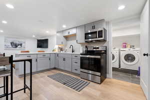 Kitchen featuring appliances with stainless steel finishes, washer and dryer, light hardwood / wood-style floors, tasteful backsplash, and gray cabinets