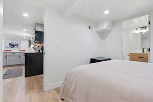 Bedroom with light hardwood / wood-style floors and beam ceiling