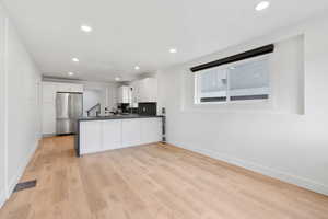 Kitchen featuring white cabinets, kitchen peninsula, light wood-type flooring, and stainless steel refrigerator