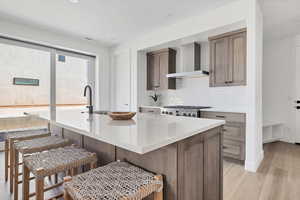 Kitchen featuring wall chimney exhaust hood, a kitchen bar, light hardwood / wood-style floors, and a kitchen island with sink