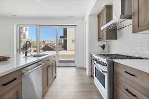 Kitchen featuring appliances with stainless steel finishes, tasteful backsplash, sink, light wood-type flooring, and wall chimney exhaust hood