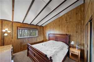 Carpeted bedroom with vaulted ceiling with beams and wood walls