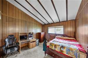 Carpeted bedroom with wood walls and vaulted ceiling with beams