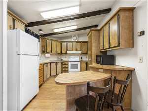 Kitchen with white fridge, kitchen peninsula, light hardwood / wood-style flooring, vaulted ceiling with beams, and range