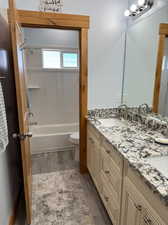 Full bathroom featuring dual vanity, toilet, LVP floors, and shower / bathtub combination