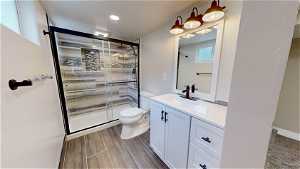 Bathroom with hardwood / wood-style floors, oversized vanity, toilet, and a shower with door