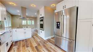 Kitchen featuring white cabinets, light hardwood / wood-style floors, island range hood, stainless steel appliances, and light stone countertops