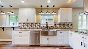 Kitchen featuring tasteful backsplash, wall chimney range hood, dishwasher, and decorative light fixtures