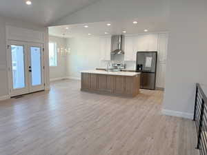 Kitchen featuring appliances with stainless steel finishes, light hardwood / wood-style floors, white cabinets, a center island with sink, and wall chimney range hood