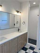 Bathroom with tile flooring, dual vanity, and a tile shower