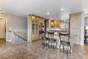 Kitchen with double oven, custom exhaust hood, light tile floors, backsplash, and a breakfast bar area