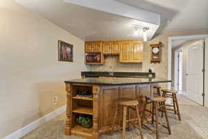 Bar with microwave, dark stone counters, light carpet, and sink