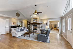 Living room with a stone fireplace, ceiling fan, light wood-type flooring, and high vaulted ceiling