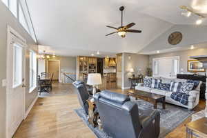 Living room featuring rail lighting, high vaulted ceiling, ceiling fan with notable chandelier, and light wood-type flooring