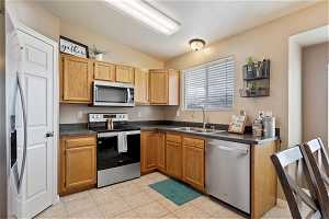 Kitchen featuring vaulted ceiling, appliances with stainless steel finishes, light tile floors, and sink