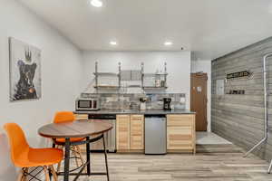 Kitchen with light wood-type flooring, light brown cabinetry, backsplash, wood walls, and appliances with stainless steel finishes