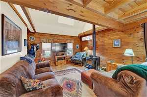 Living room featuring light hardwood / wood-style floors, a skylight, an AC wall unit, beamed ceiling, and a wood stove
