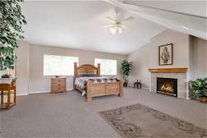 Carpeted bedroom featuring lofted ceiling, a fireplace, and ceiling fan