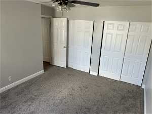 Unfurnished bedroom with dark colored carpet, ceiling fan, and multiple closets
