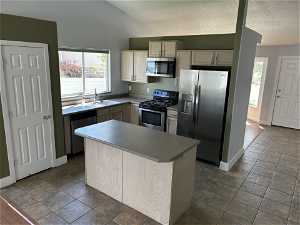 Kitchen with tile floors, stainless steel appliances, sink, a kitchen island, and lofted ceiling
