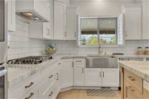 Kitchen featuring tasteful backsplash, custom exhaust hood, white cabinets, sink, and light wood-type flooring