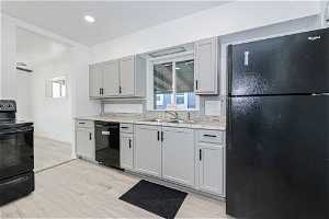 Kitchen with a wealth of natural light, light hardwood / wood-style flooring, sink, and black appliances