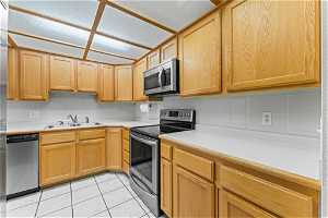 Kitchen with tasteful backsplash, appliances with stainless steel finishes, light tile floors, and sink
