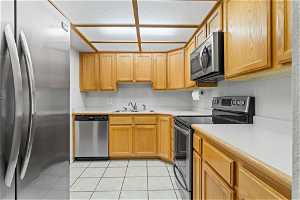 Kitchen with sink, backsplash, appliances with stainless steel finishes, and light tile floors