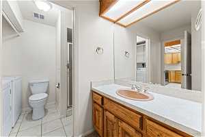 Bathroom with toilet, tile flooring, an enclosed shower, independent washer and dryer, and vanity