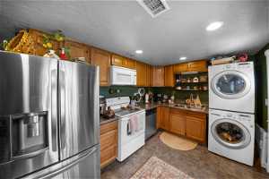Kitchen with sink, appliances with stainless steel finishes, dark tile floors, and stacked washing maching and dryer