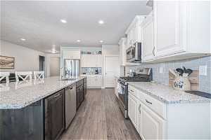Kitchen with appliances with stainless steel finishes, white cabinets, light hardwood / wood-style floors, tasteful backsplash, and an island with sink