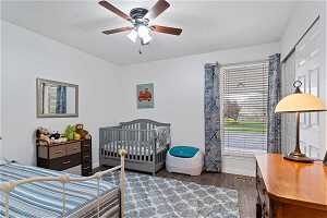 Bedroom featuring ceiling fan, dark hardwood / wood-style flooring, and a nursery area
