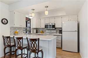 Kitchen featuring kitchen peninsula, hanging light fixtures, white appliances, light hardwood / wood-style floors, and sink