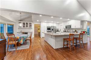 Kitchen with appliances with stainless steel finishes, light hardwood / wood-style flooring, vaulted ceiling, white cabinetry, and pendant lighting