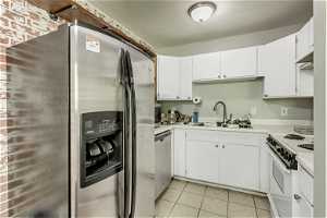 Kitchen featuring light tile floors, appliances with stainless steel finishes, white cabinetry, and sink