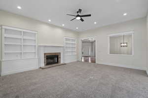 Unfurnished living room featuring ceiling fan with notable chandelier, a fireplace, carpet floors, and built in features