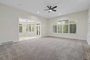 Unfurnished room featuring ceiling fan with notable chandelier and light carpet