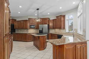 Kitchen with hanging light fixtures, a kitchen island, black appliances, tasteful backsplash, and sink