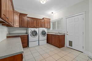 Laundry area featuring sink, cabinets, separate washer and dryer, and light tile floors