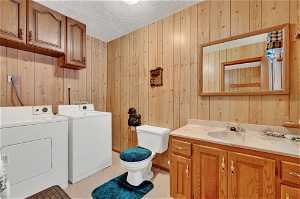 Bathroom featuring large vanity, a textured ceiling, independent washer and dryer, wooden walls, and toilet