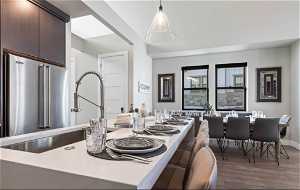 Interior space with hardwood / wood-style flooring, high end fridge, dark brown cabinets, and hanging light fixtures