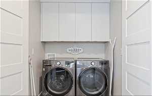 Clothes washing area with washer and clothes dryer, cabinets, and washer hookup