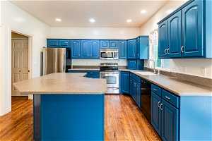 Kitchen with a kitchen island, light wood-type flooring, stainless steel appliances, sink, and blue cabinets