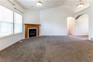 Living room with plenty of natural light, vaulted ceiling, carpet, and a tile fireplace with wood mantel