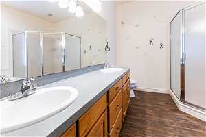 Bathroom featuring vanity with extensive cabinet space, toilet, hardwood / wood-style flooring, walk in shower, and double sink